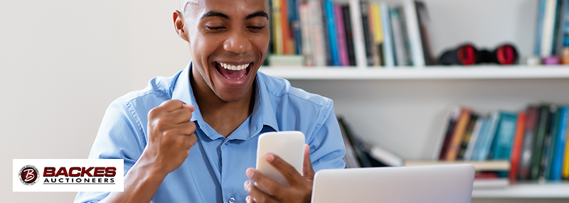 Image for Happy young man holding his phone and raising a fist due to excitement